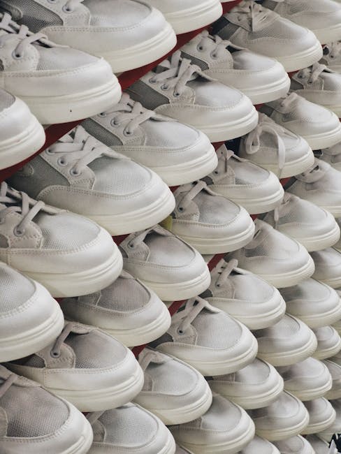 Close-up view of multiple pairs of white and gray sneakers arranged on a retail display shelf. The sneakers are stacked in rows, with some pairs leaning slightly to the side, showing details of their fabric, laces, and soles. The shoes appear to be new and are stored in an organized manner, typical of a footwear retail environment. This image highlights the ease of handling and moving lightweight footwear during home or commercial relocations, which [Company Name] manages as part of their house removal and furniture transport services. The photograph emphasizes the importance of careful packing and handling during packing and moving processes, aligning with the services offered by [COMPANY_NAME]. The setting has neutral lighting, with the sneakers occupying the foreground and background, showcasing the variety and quantity of footwear that may be involved in household or business relocations. The scene reflects the types of items that can be efficiently packed, moved, and transported by professional removals specialists.